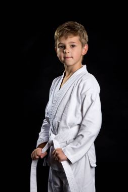 Karate çocukta siyah arka plan üzerine poz yepyeni kimono, gülümseyen. Onun kemer tutarak karate avcı