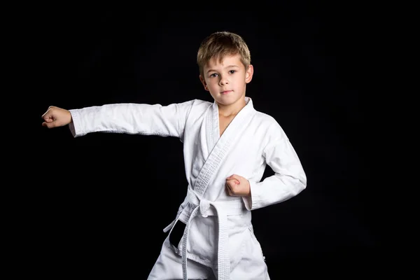 Straight karate arm hit. Kid in brand new kimono looking on the camera on isolated black background — Stock Photo, Image