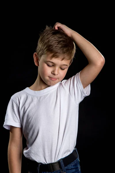 Bambino pentito, ragazzo intelligente sullo sfondo nero con una mano sulla testa e la testa piegata. Emozioni di bambini . — Foto Stock