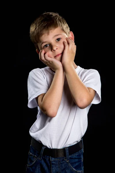 Retrato bonito menino com palmas segurando nas bochechas no fundo preto — Fotografia de Stock