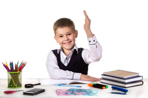 Sonriente alumno alegre excelente con la mano arriba sentado en la mesa sobre el fondo blanco — Foto de Stock