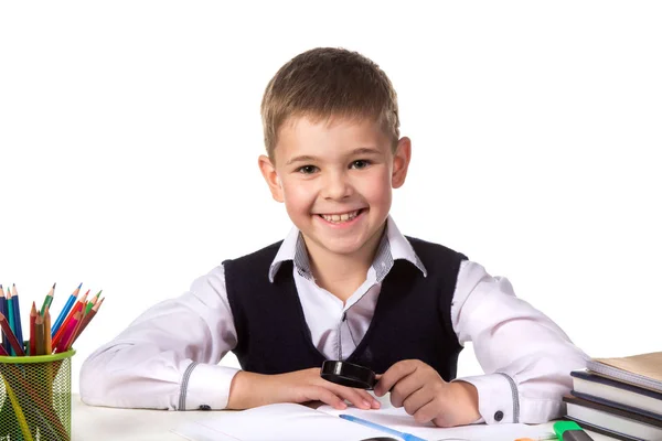 Sonriente alumno excelente con lupa de exploración sentado en la mesa sobre el fondo blanco — Foto de Stock