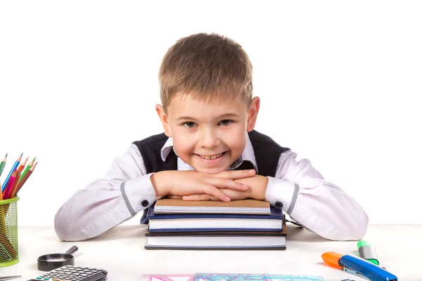 Alumno sonriente sentado en el escritorio con la cabeza sobre la pila de libros rodeados de papelería —  Fotos de Stock