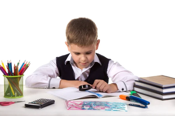 Smart serious pupil at the desk exploring with magnifier on the clean white background Stock Image