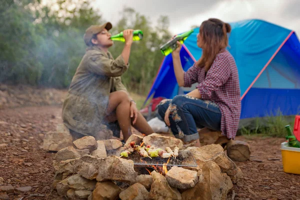 Happy friends camping party and enjoying bonfire in nature and lake, Traveler camping on the river/mountain. With a relaxing drink in the sunset. The concept of hiking/camping and relax. Closeup.