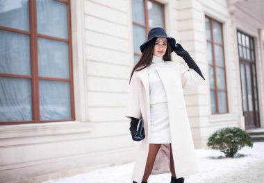 Sevimli genç kadın ceket uzun esmer saçlı büyük şehirde kar yağışı zevk bir şapka giymiş. Neşeli duygular, gülümseyen, Noel ruh hali, pozitif yüz duygular, kış hava. Deri eldiven ve şık çanta.