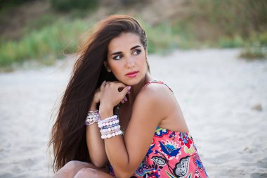 Güzel esmer kız bir sahil üzerinde poz. Şık takı. 