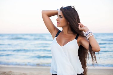 Güzel esmer kız bir sahil üzerinde poz. Şık takı. 