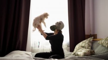 Gaz maskeli bir kadın yatakta bir köpekle oynuyor.