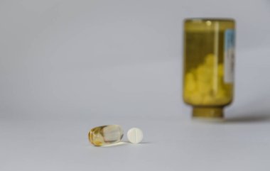 Sağdaki ayakta duran şişenin arka planında hap ve kapsül var..