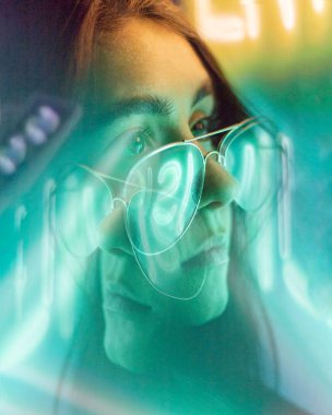 Siyah saçlı, şeffaf gözlüklü bir kız, yansımalı neon renkli bir fotoğraf.