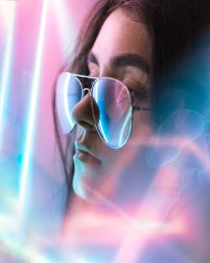 Siyah saçlı, şeffaf gözlüklü bir kız, yansımalı neon renkli bir fotoğraf.