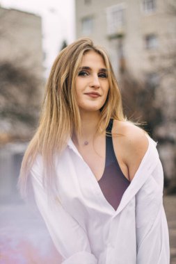 Beş katlı bir apartmanın arka planında beyaz gömlekli sarı saçlı genç bir kızın portresi.