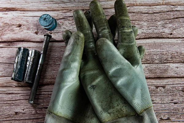 Dirty gloves and work tools on wooden background