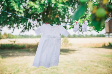 Bahçedeki çamaşır ipinde asılı beyaz bebek kıyafetleri ağaçların arka planında