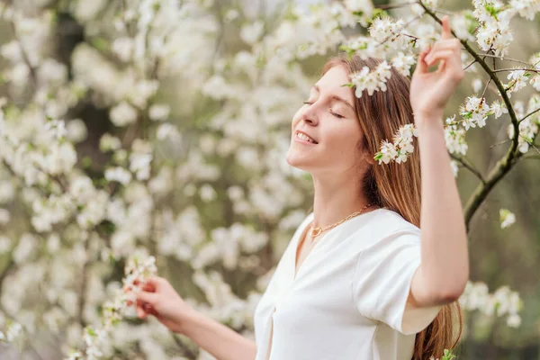 portrait of a girl in a white blouse of the European race in a blossoming cherry in the spring. happy smiling girl. selective focus and place for text. spring mood; happiness