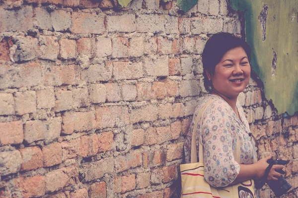 Asia mujer sosteniendo una cámara de pie contra una pared de ladrillo — Foto de Stock