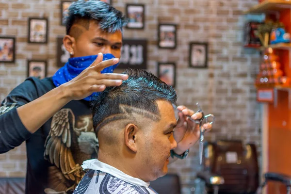 Barbeiro corte de cabelo de um cliente na barbearia — Fotografia de Stock