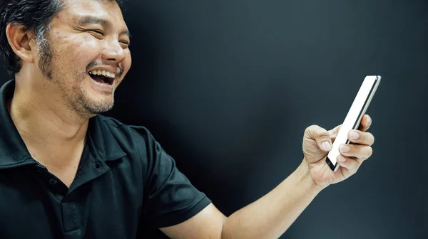 Azjatycki człowiek uśmiechający się za pomocą smartfona w mrocznym klimacie — Zdjęcie stockowe