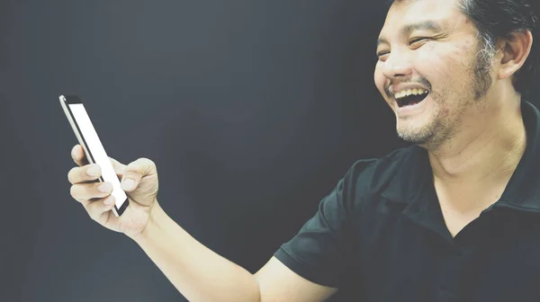Azjatycki człowiek uśmiechający się za pomocą smartfona w mrocznym klimacie — Zdjęcie stockowe