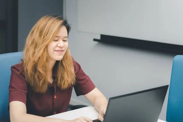 Asian woman is student, businesswoman working by computer notebook, laptop in office meeting room with whiteboard in background with happy and relax emotion in concept working woman, success in life