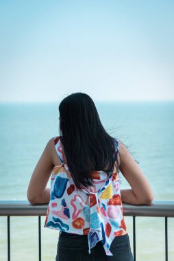 Asyalı güzel kadın deniz manzarasında rahatlıyor. Konsept seyahat, tatil, hayattaki eğlence gibi mutlu ve eğlenceli duygularla.