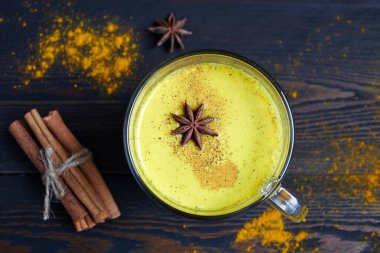 Geleneksel Hint içkisi zerdeçal latte ya da tarçınlı altın süt, yıldız anason ve sade ahşap masa üzerinde zerdeçal..