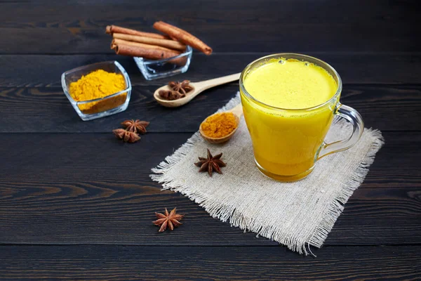 Geleneksel Hint içkisi zerdeçal latte ya da tarçınlı altın süt, yıldız anason ve sade ahşap masa üzerinde zerdeçal..