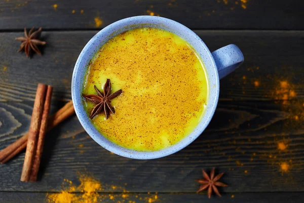 Golden milk is the traditional Indian turmeric drink with spices on dark rustic wooden background.