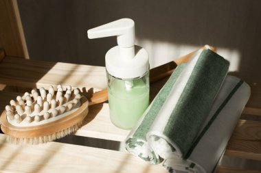 Banyodaki aksesuarlar bir rafta duruyor, antiselülit fırça, sıvı sabun, havlular.