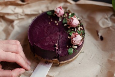 El pastayı bir bıçakla keser. Mor pasta. Pasta çiçeklerle süslenmiş.. 