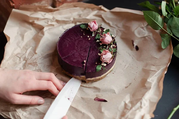 The hand cuts the cake with a knife. Purple cake. The cake is decorated with flowers.