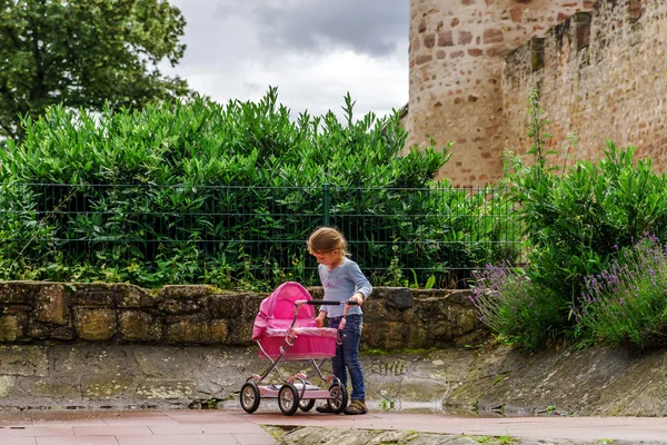 Schattig klein meisje met pop en babycarrier in het park spelen — Stockfoto