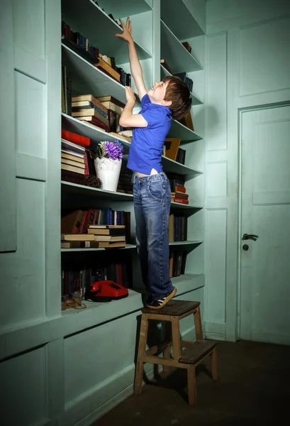 Niño pecoso de pelo rojo buscando libro en la estantería — Foto de Stock