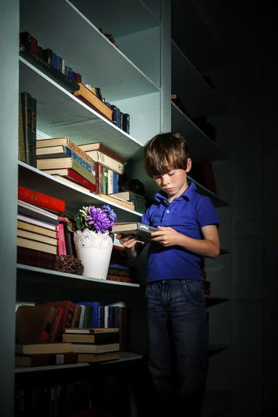 Piegowaty rudy chłopiec wyszukiwanie książki na Regał — Zdjęcie stockowe