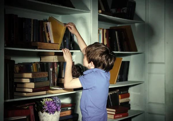 脸上有雀斑红头发的小男孩，搜索在书架上的书 — 图库照片