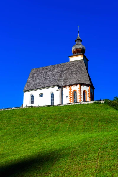 Mooie kerkje in de Alpen. Zonnige dag, groen gras op de h — Stockfoto