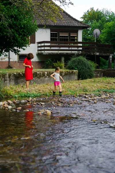 Madre con hija cruzando el pequeño río —  Fotos de Stock