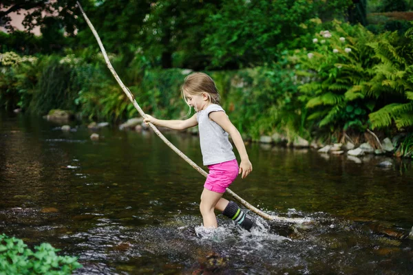 Nettes kleines Mädchen überquert Fluss mit Stock — Stockfoto