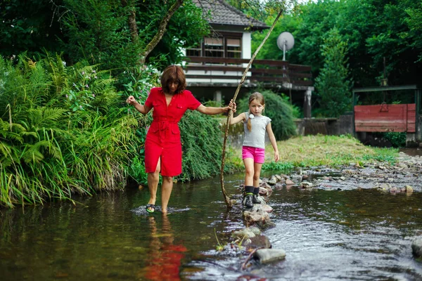 Madre con hija cruzando el pequeño río —  Fotos de Stock