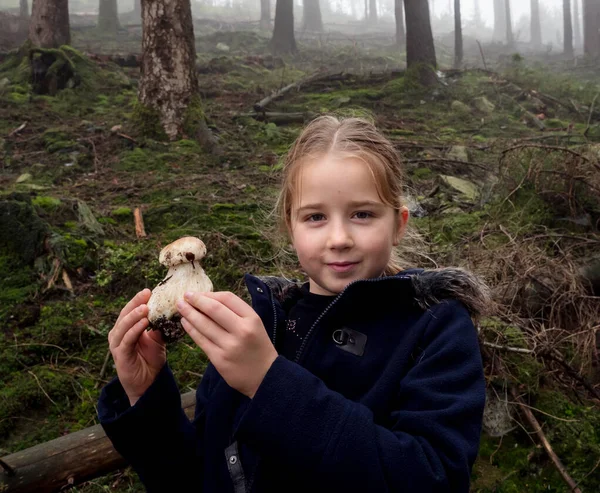 Kleines Mädchen zeigt einen weißen Pilz, der gerade im Vordergrund gefunden wurde — Stockfoto