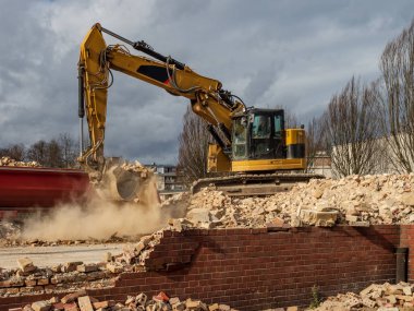 An excavator breaks down an old building. Dust, bricks and broke