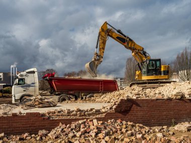 An excavator breaks down an old building. Dust, bricks and broke