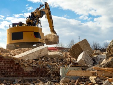 An excavator breaks down an old building. Dust, bricks and broke