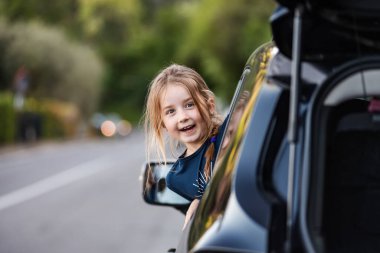 Küçük komik kız, arabanın camından sarkıyor. Aile seyahati.