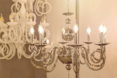 Metal krom armatürler ve mum şeklinde gölgelerle parlayan bir lamba görüntüsü. İç mekandaki klasik tarz kavramı. Kapatın. Yumuşak sıcak filtre, seçici odak.