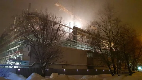 Night work on the construction of new housing for young families. Builders work on the scaffolding. Buying an apartment in a residential building.