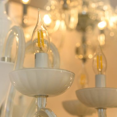 Klasik dekoratif avizenin kristaline yakın, tavan üzerine monte edilmek üzere tasarlanmış dallanmış bir süs lambası armatürü. Yumuşak sıcak filtre, seçici odaklanma. Kapalı alanda. Beyaz parlak cam..