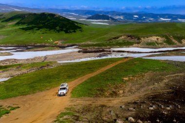 Beyaz spor araç dağlarda off-road yapıyor. Yaz, güneşli hava. Kamçatka, Rusya. Panoramik karlı manzara. Yüksek puanlı atış.