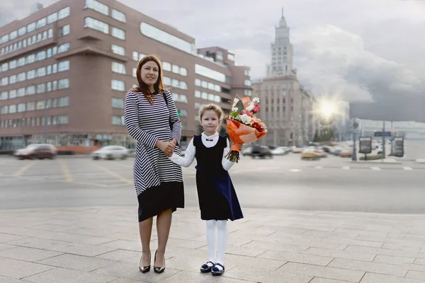 Anne ve kızı el ele tutuşup sokak manzarasında dikiliyorlar. Bilgi günü. Elinde bir buket çiçek tutan bir kız. Tünaydın..